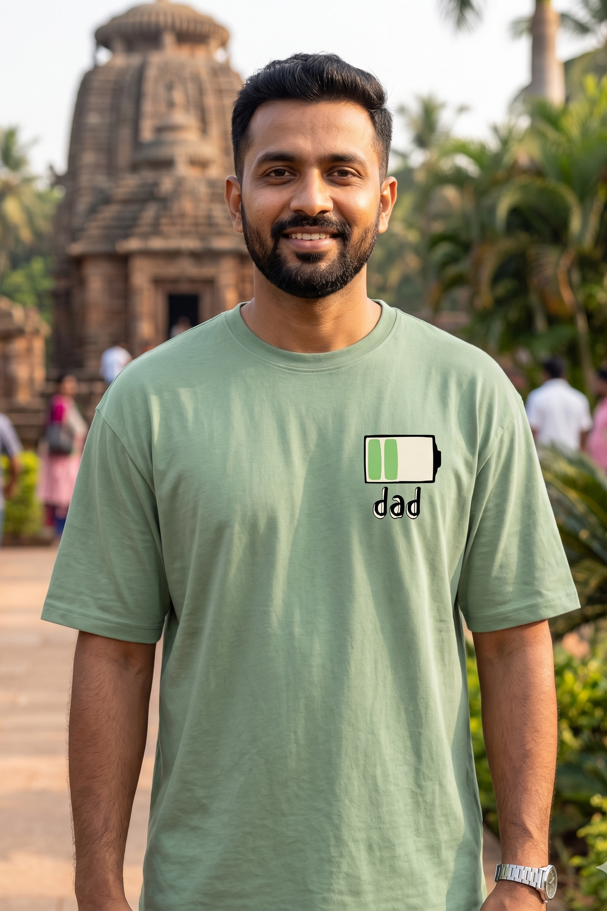 Man wearing a green t-shirt with 'dad' and a battery icon in front of a temple.