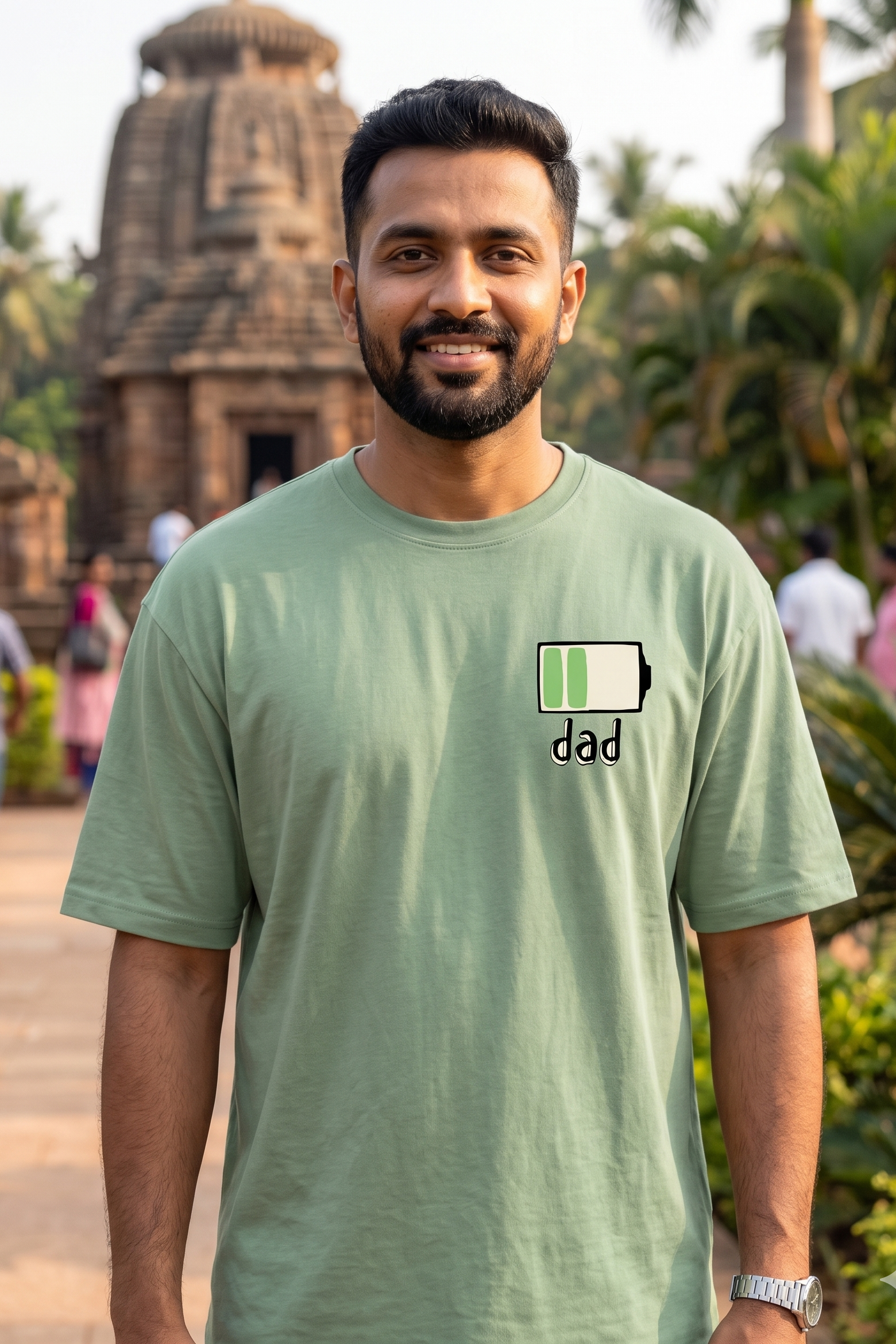 Man wearing a green t-shirt with 'dad' and a battery icon in front of a temple.