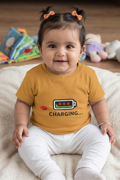 Child wearing a yellow shirt with a battery charging graphic and text, sitting on a soft surface with toys in the background.