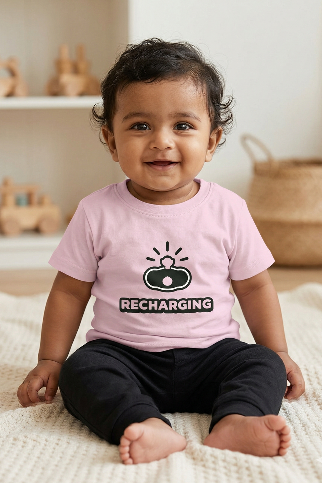 Child wearing a pink shirt with a 'Recharging' graphic sitting on a rug.