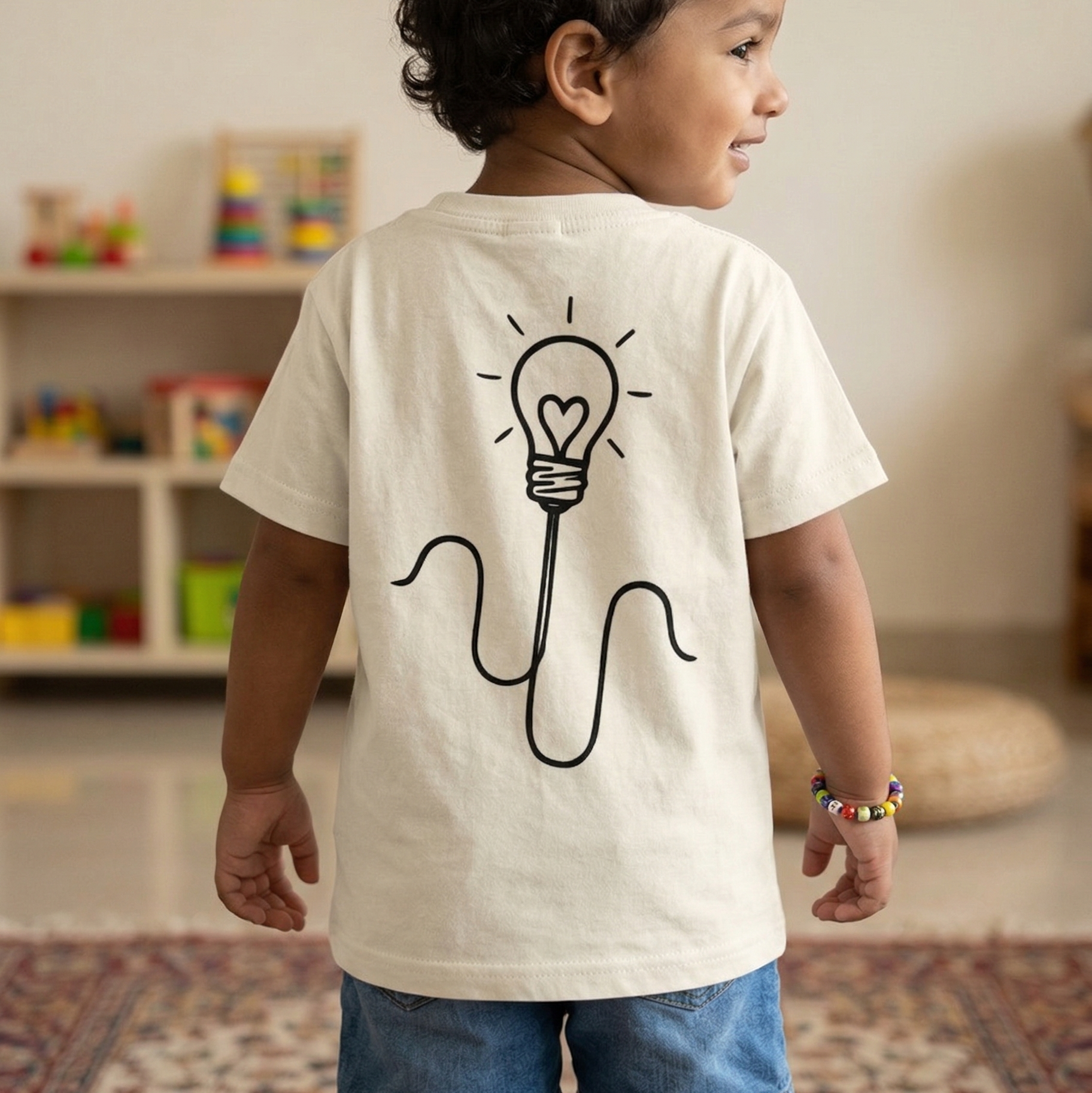Child wearing a white t-shirt with a light bulb design in a room with toys on a shelf.