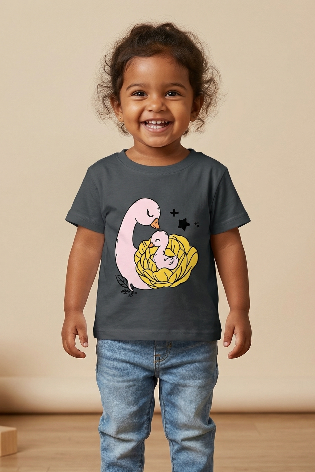 Child wearing a dark gray t-shirt with a colorful graphic design of baby and mumma duck, standing on a wooden floor.