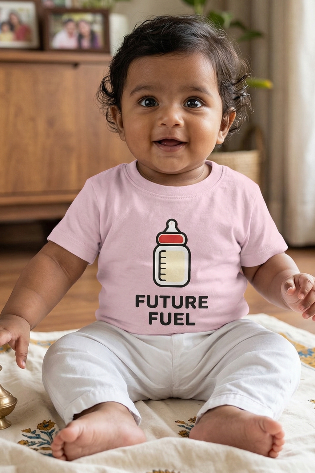 Baby wearing a pink shirt with a baby bottle graphic and 'Future Fuel' text, sitting on a patterned rug.