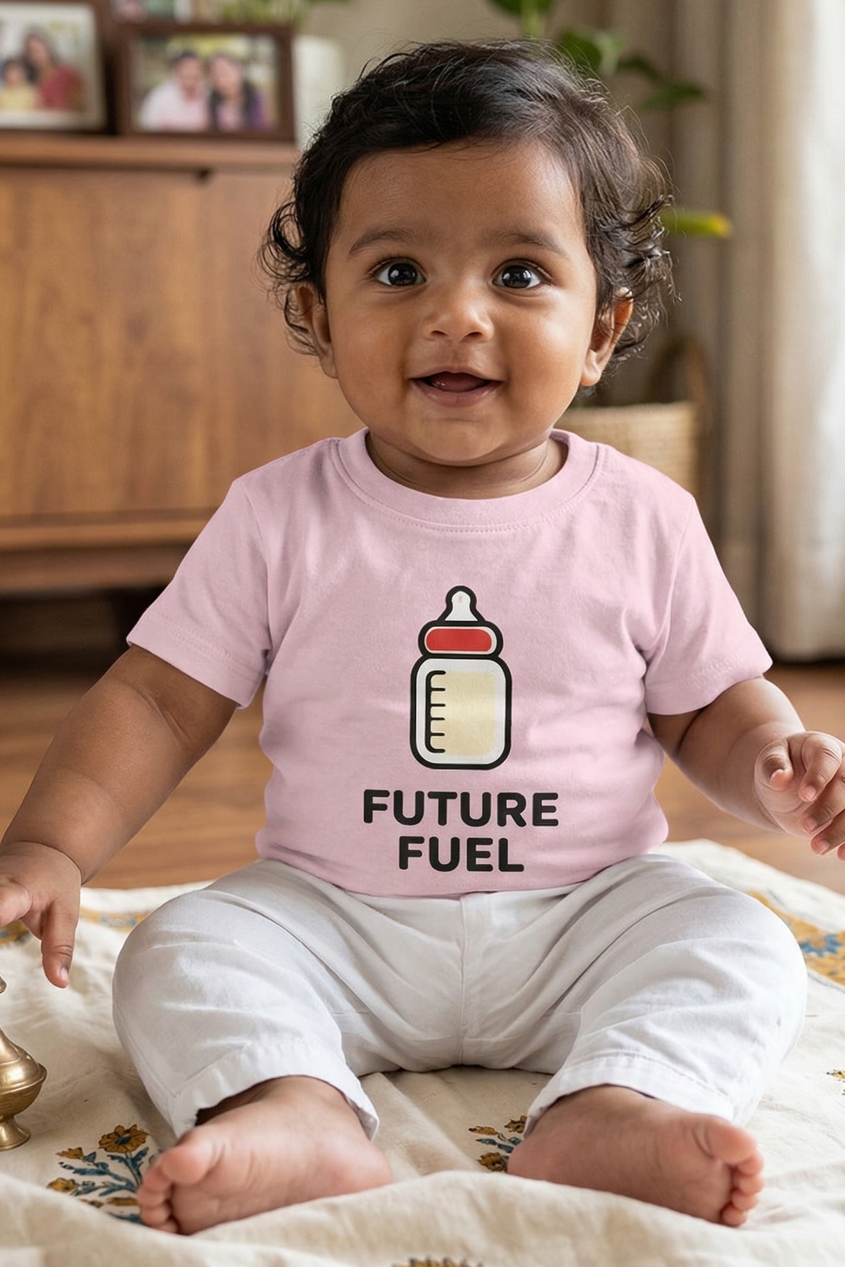 Baby wearing a pink shirt with a baby bottle graphic and 'Future Fuel' text, sitting on a patterned rug.