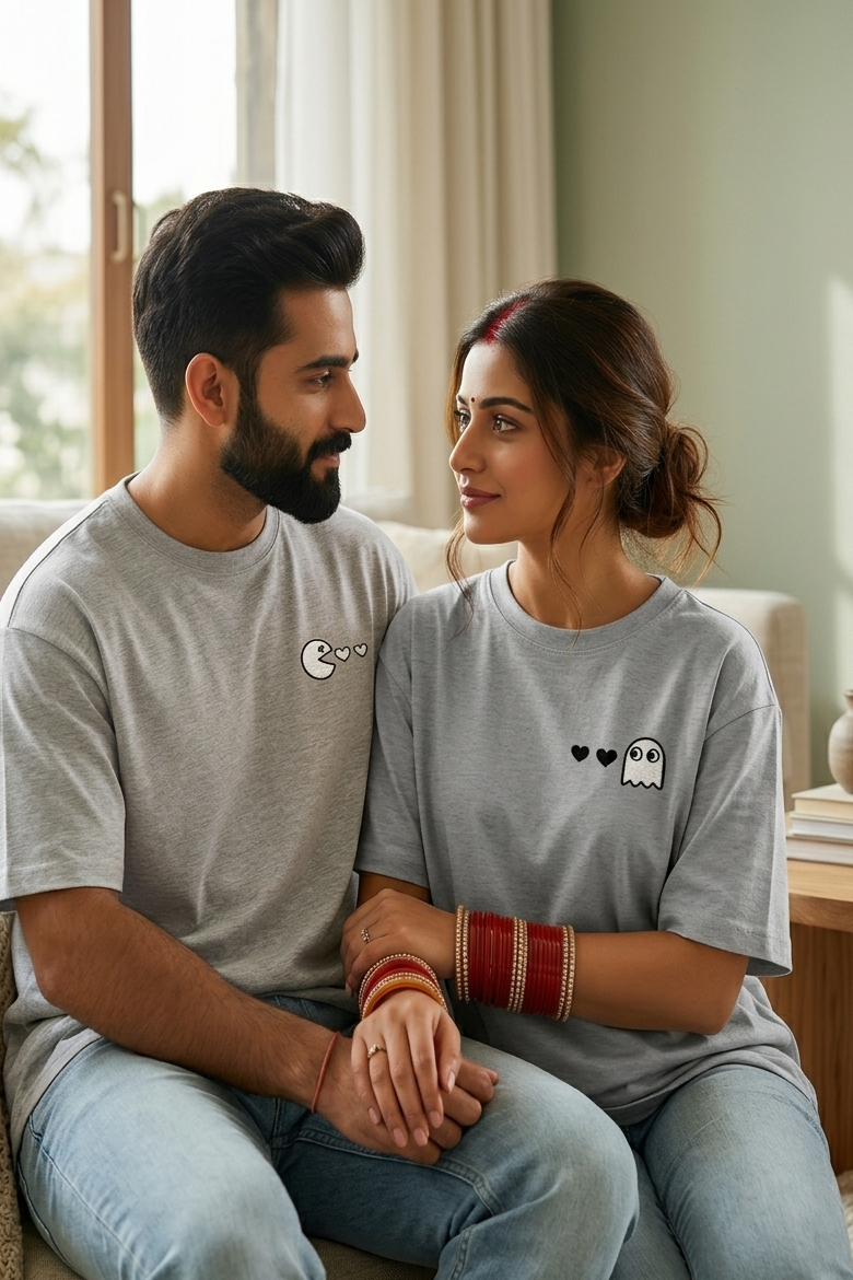 Man and woman sitting together in a cozy living room, wearing matching gray t-shirts with small designs.