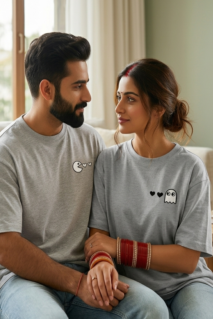 Man and woman sitting together in a cozy living room, wearing matching gray t-shirts with small matching designs.