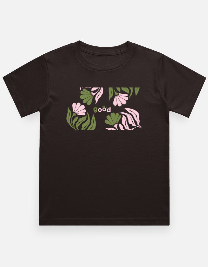 A dark brown short-sleeve t-shirt with a graphic print on the chest featuring pink flowers, green leaves, and the word 'good' in white, displayed on a light gray background.