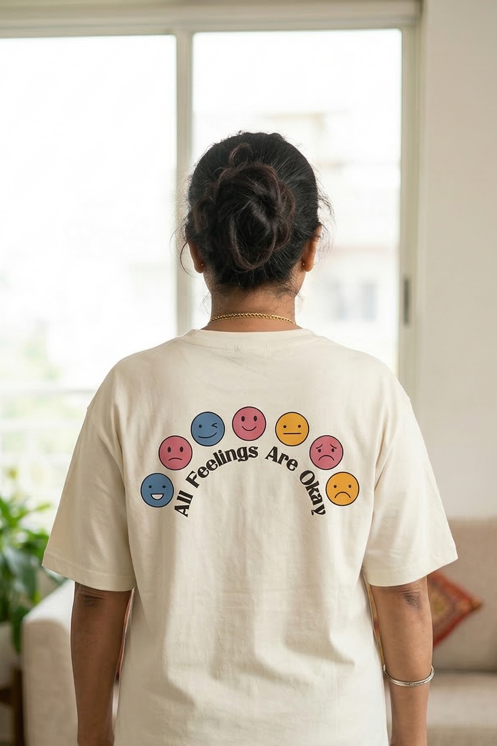 Person wearing a white t-shirt with colorful smiley face designs and text in a living room.