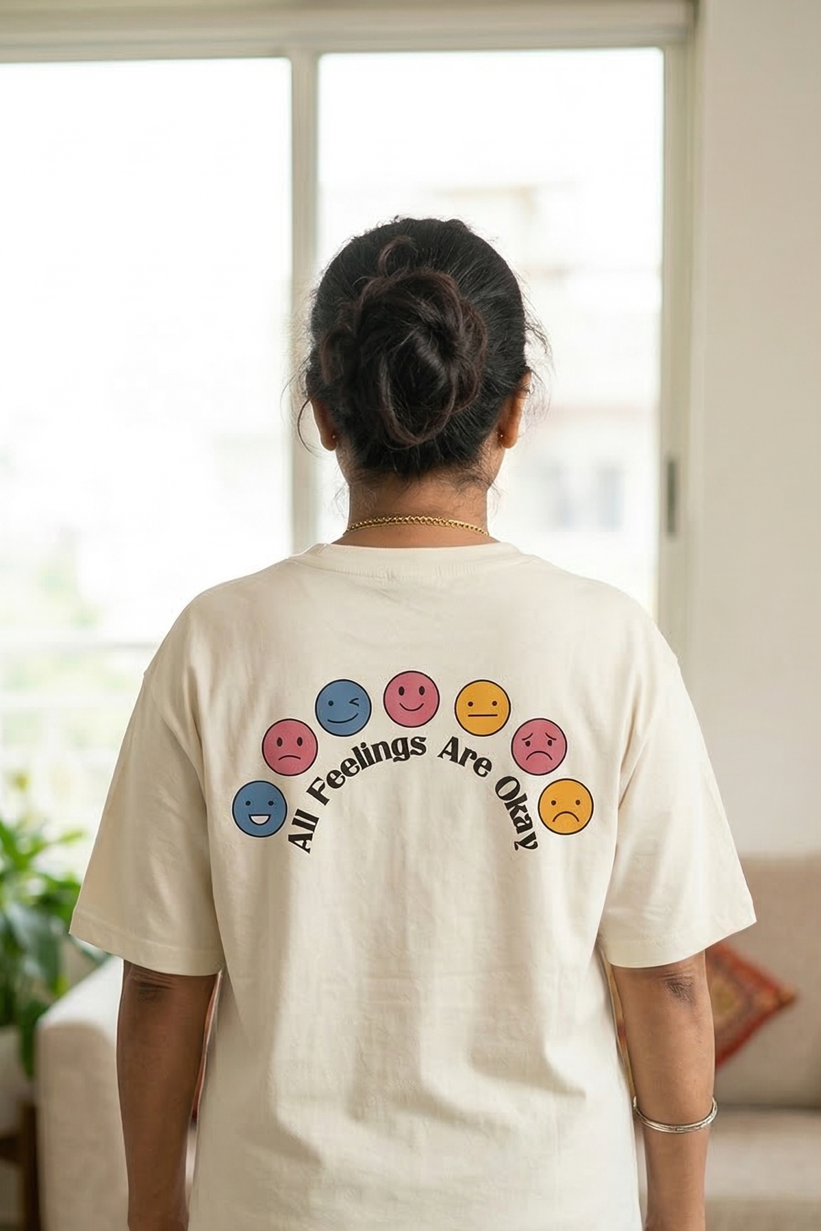 Person wearing a white t-shirt with colorful smiley face designs and text in a living room.