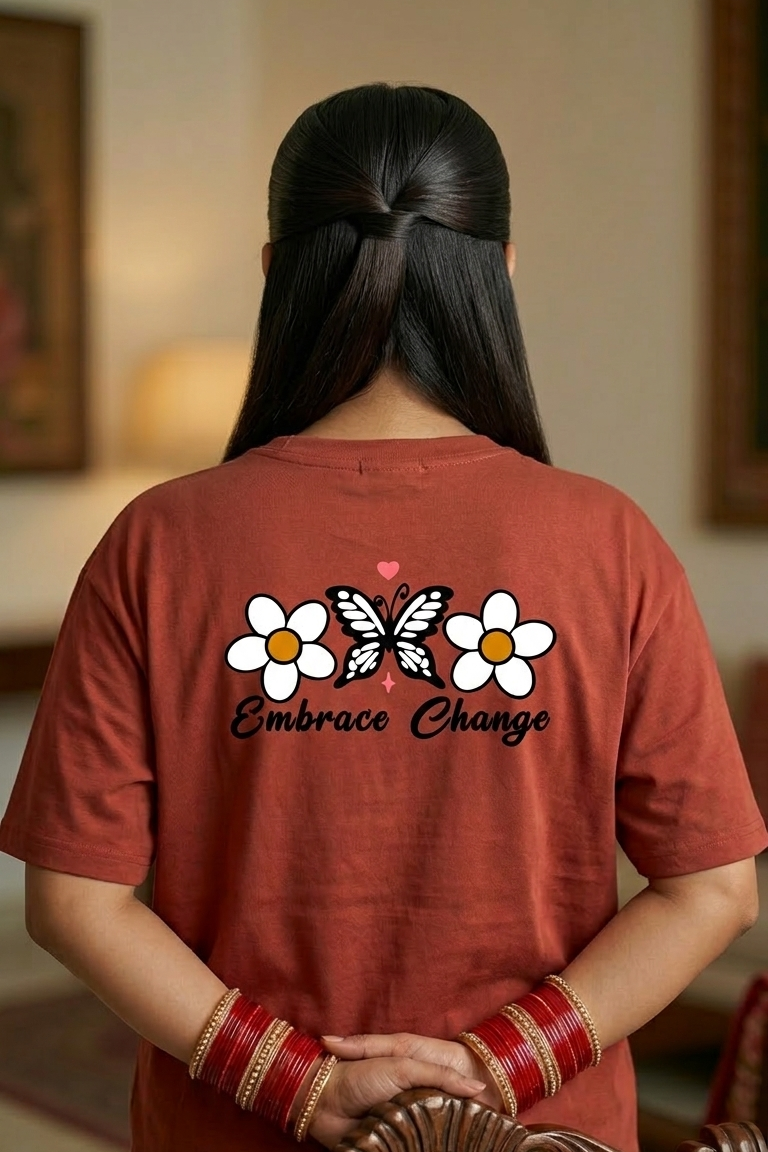 Person wearing a red t-shirt with a butterfly and flower design on the back, sitting on a wooden chair.