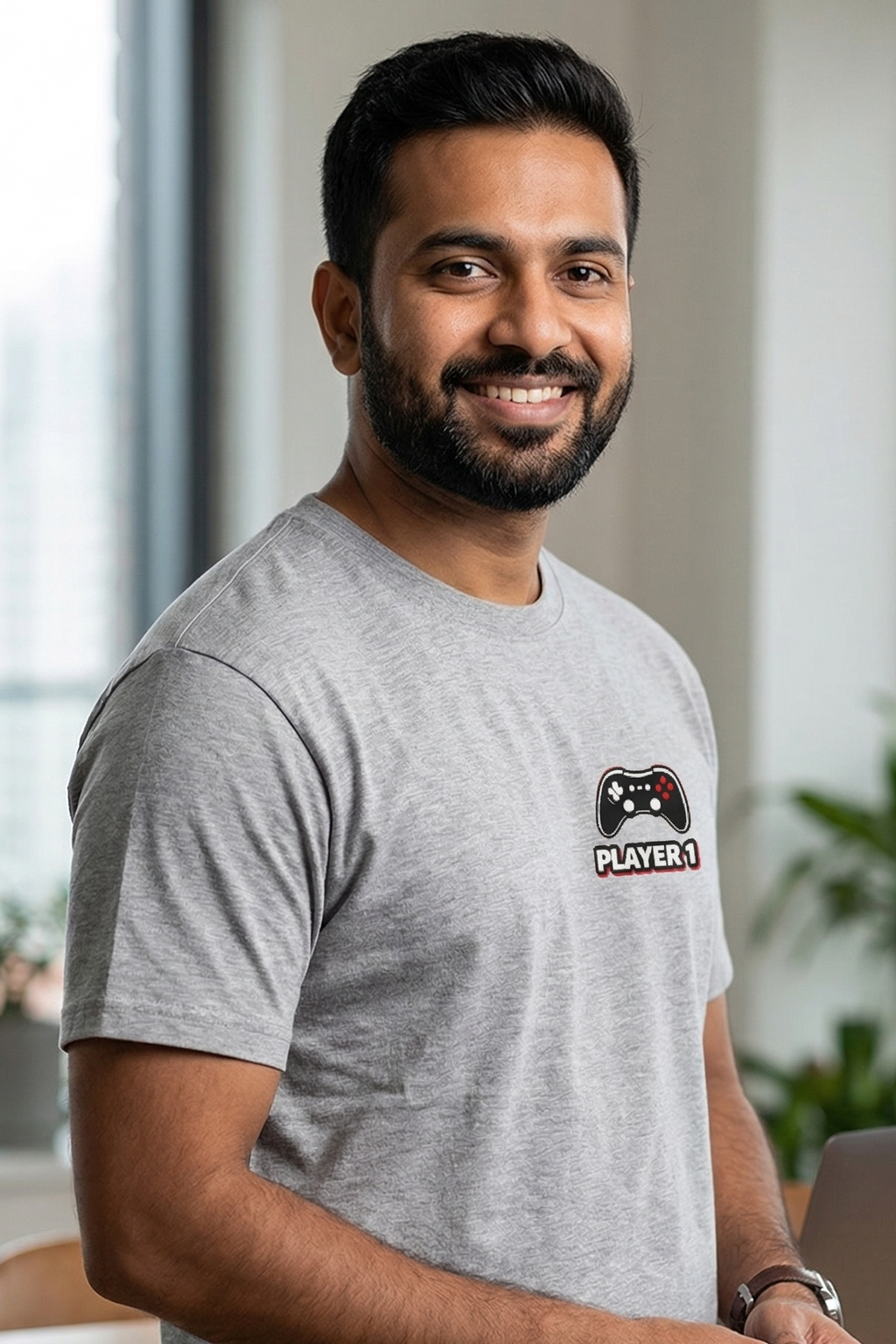 Man wearing a gray t-shirt with a logo, standing in an office setting.
