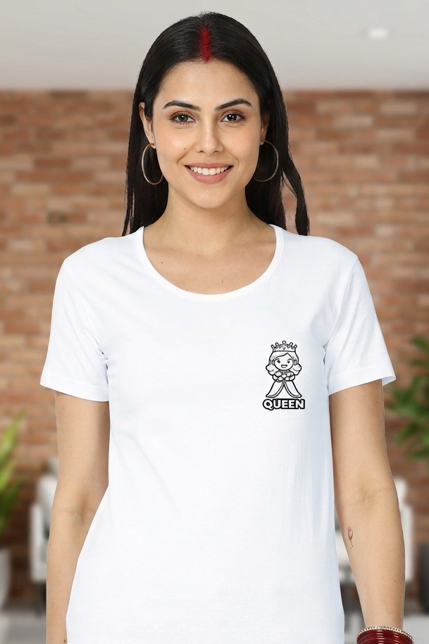 Woman wearing a white t-shirt with a queen logo and text, standing in a room with plants and a brick wall.